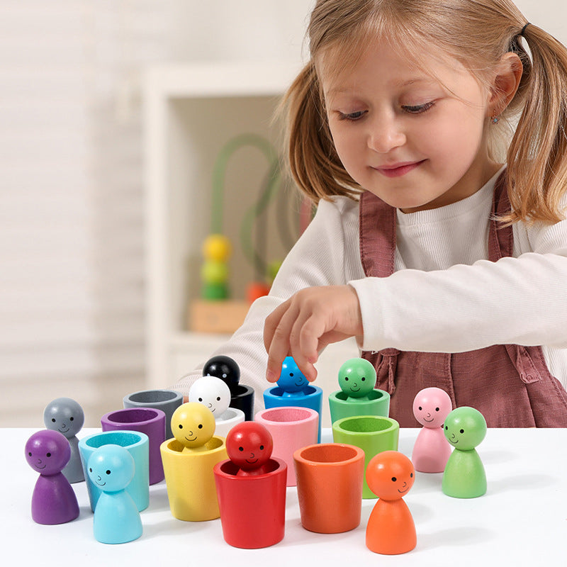 Child matching a blue wooden figure to a blue cup among colorful sorting pieces