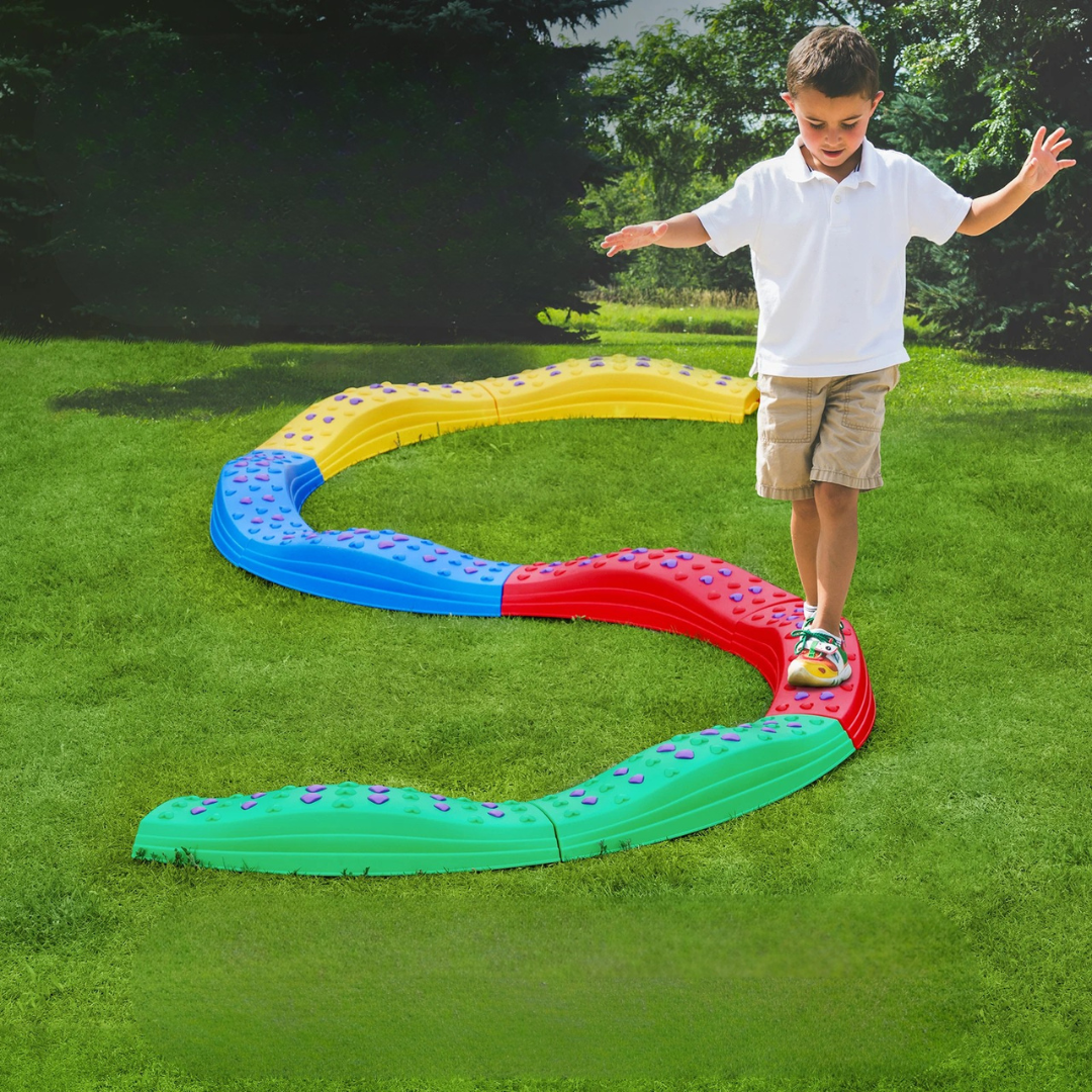 Child balancing on a winding multicolor balance beam in a grassy yard