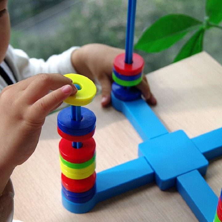 Child placing a yellow magnetic ring onto a blue post above other colored rings