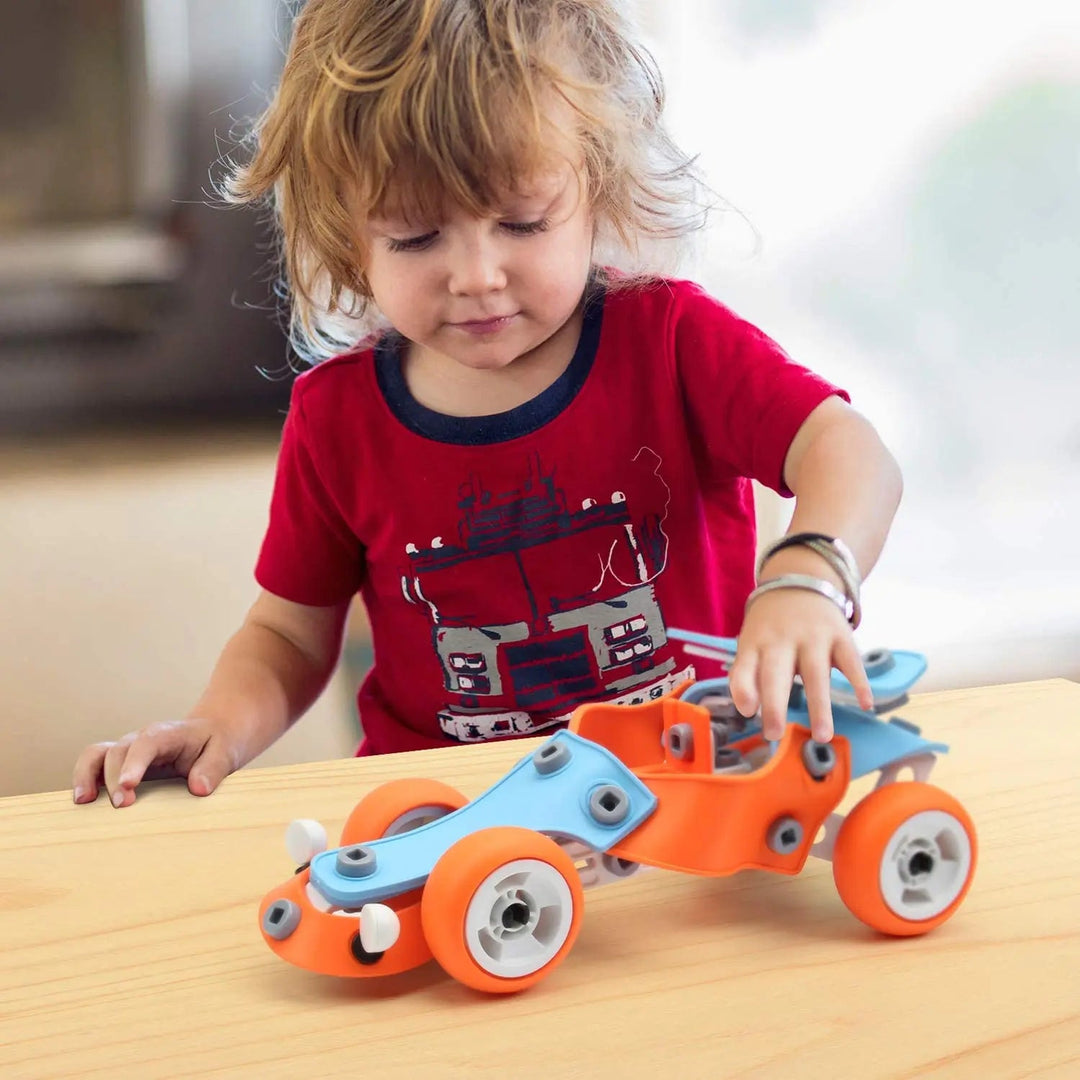 Child playing with a blue and orange construction car on a wooden table
