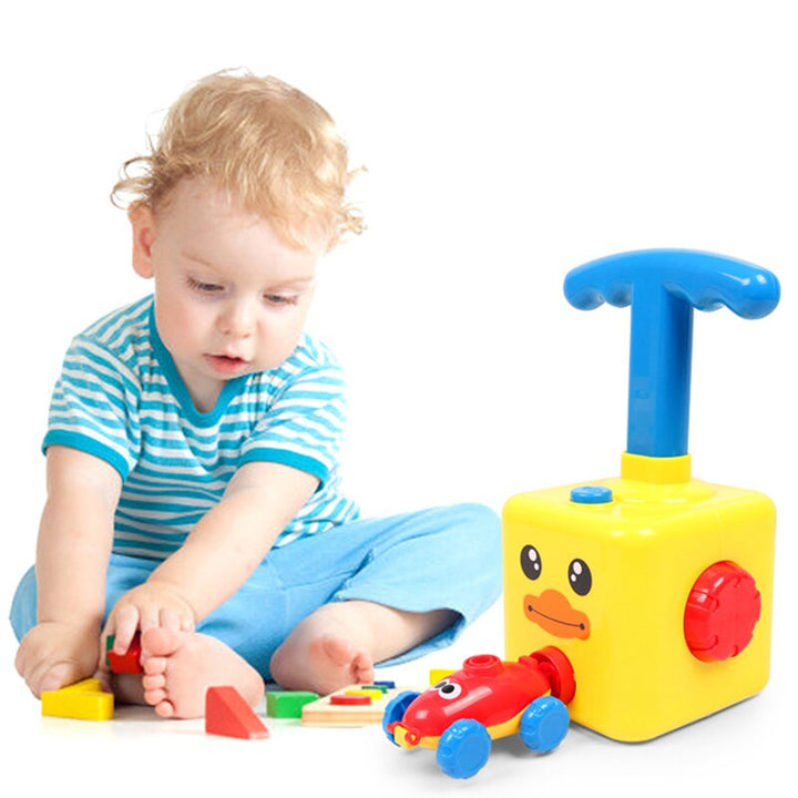 Child playing with a red balloon car beside a yellow pump with a blue handle
