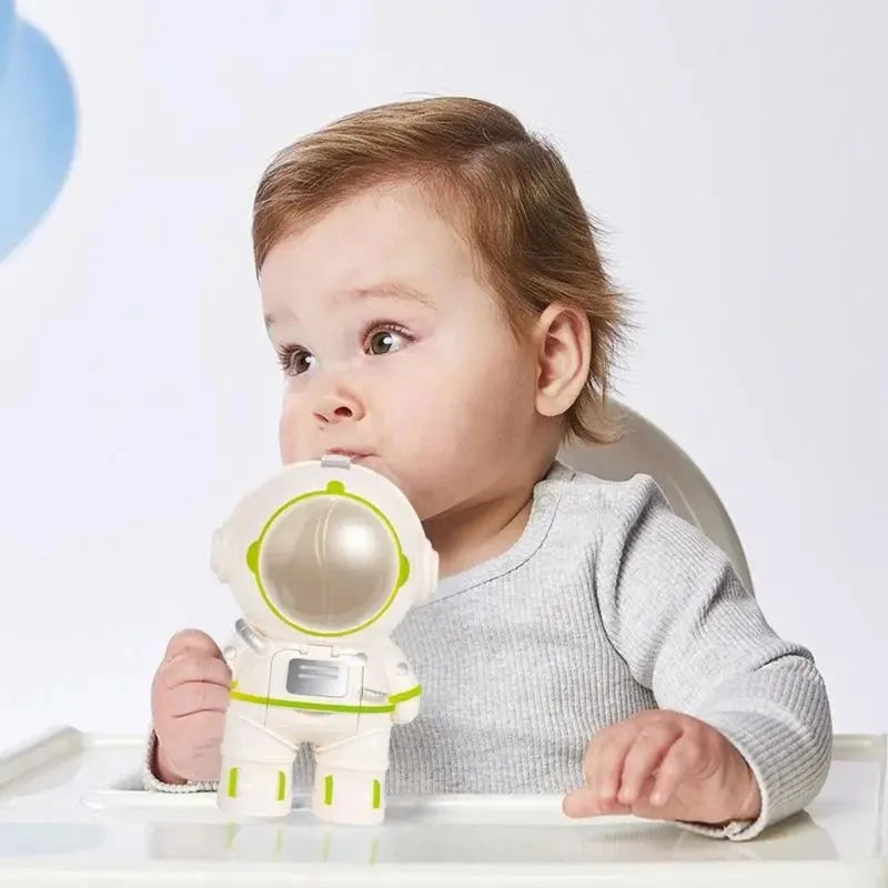 A child sipping from a white astronaut water bottle while seated at a high chair.
