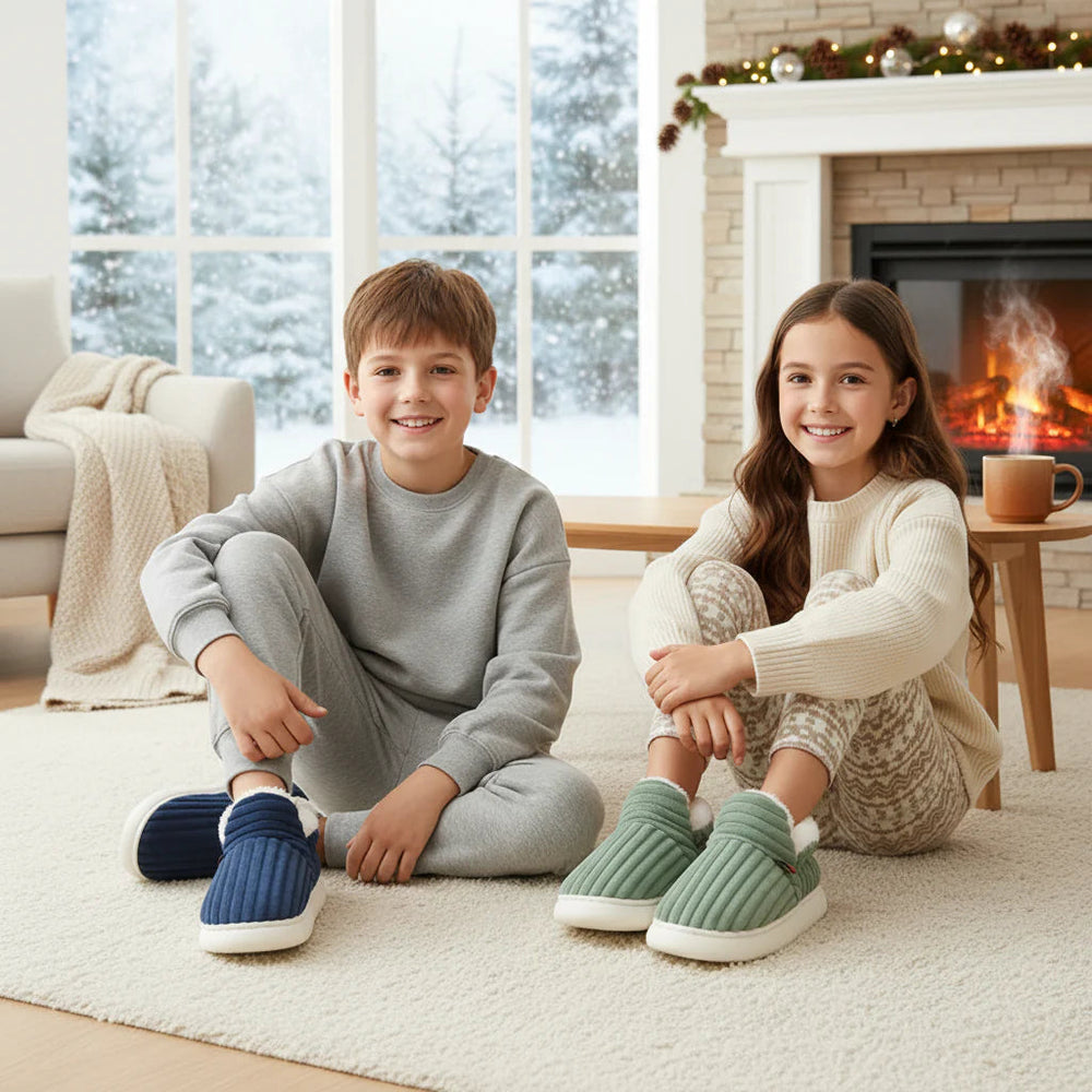 Two children wearing blue and green corduroy slippers beside a fireplace.