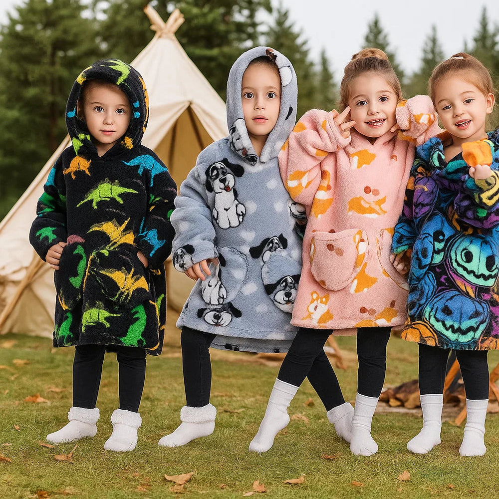 Four children wearing patterned hooded blankets outdoors beside a tent