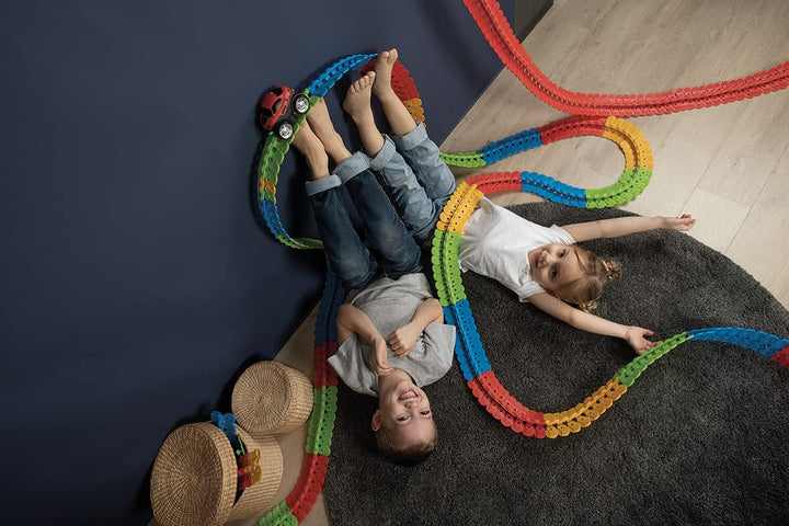 Two children lying beside a winding multicolor race track on the floor