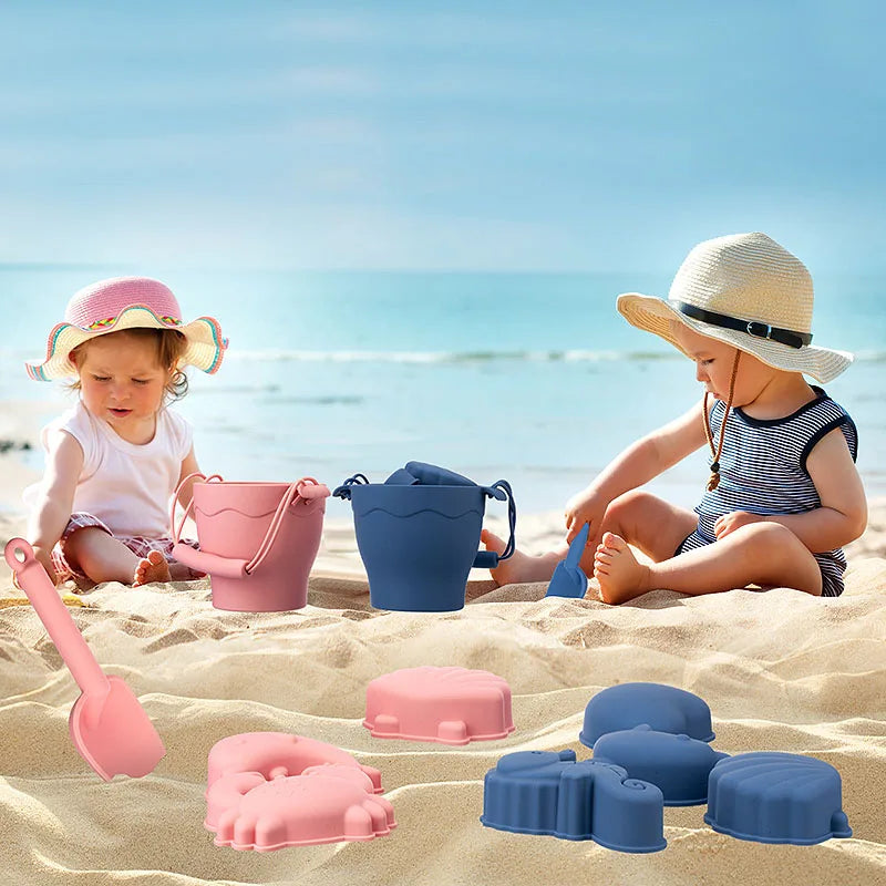 Two children playing on the beach with pink and blue buckets, shovels and sand molds.
