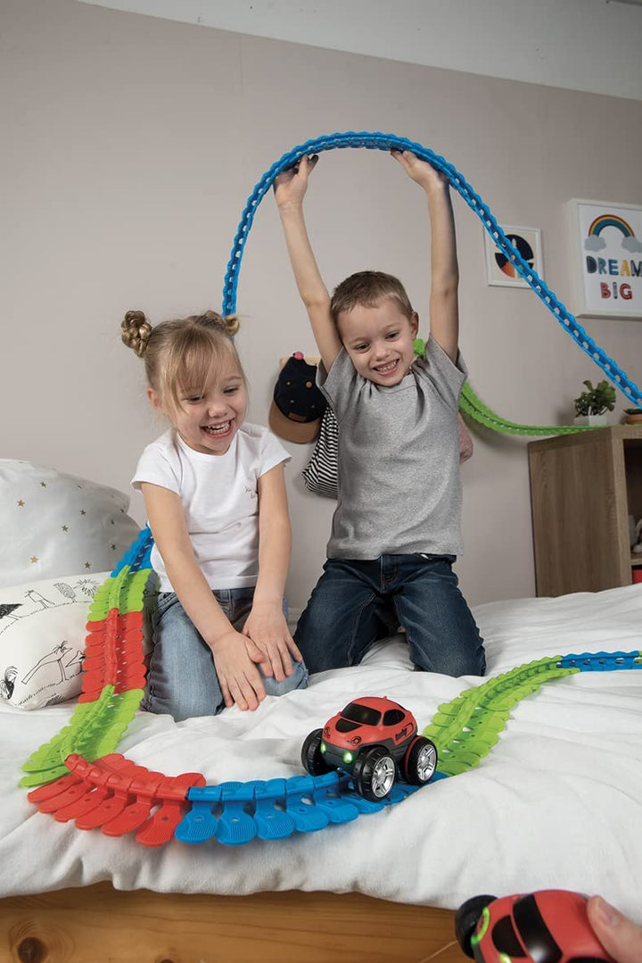 Two children shaping a tall flexible track arch above a race track on a bed