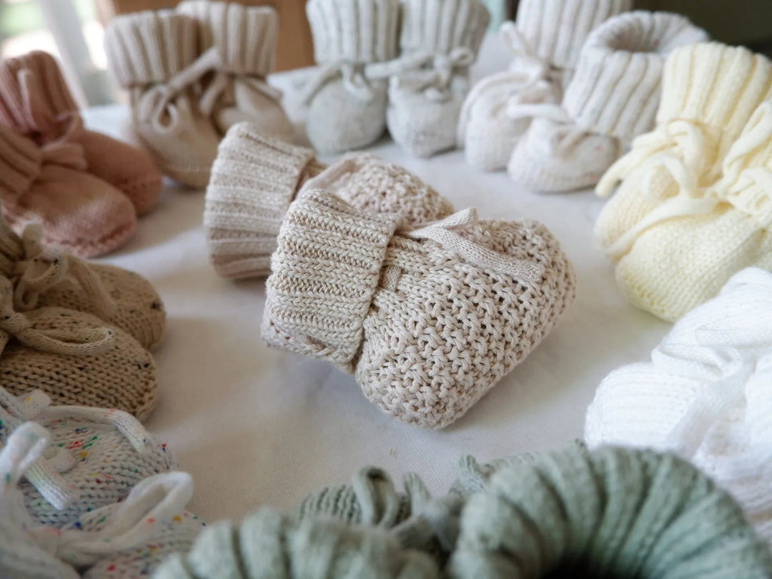 A folded-cuff baby bootie showing its textured knit, surrounded by other color options.