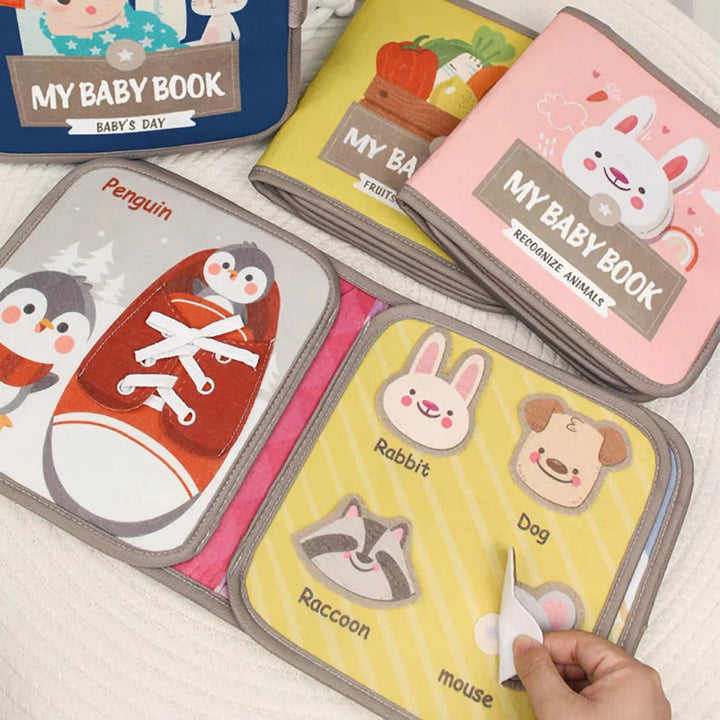 Open cotton busy books showing a penguin lacing activity and removable animal pieces