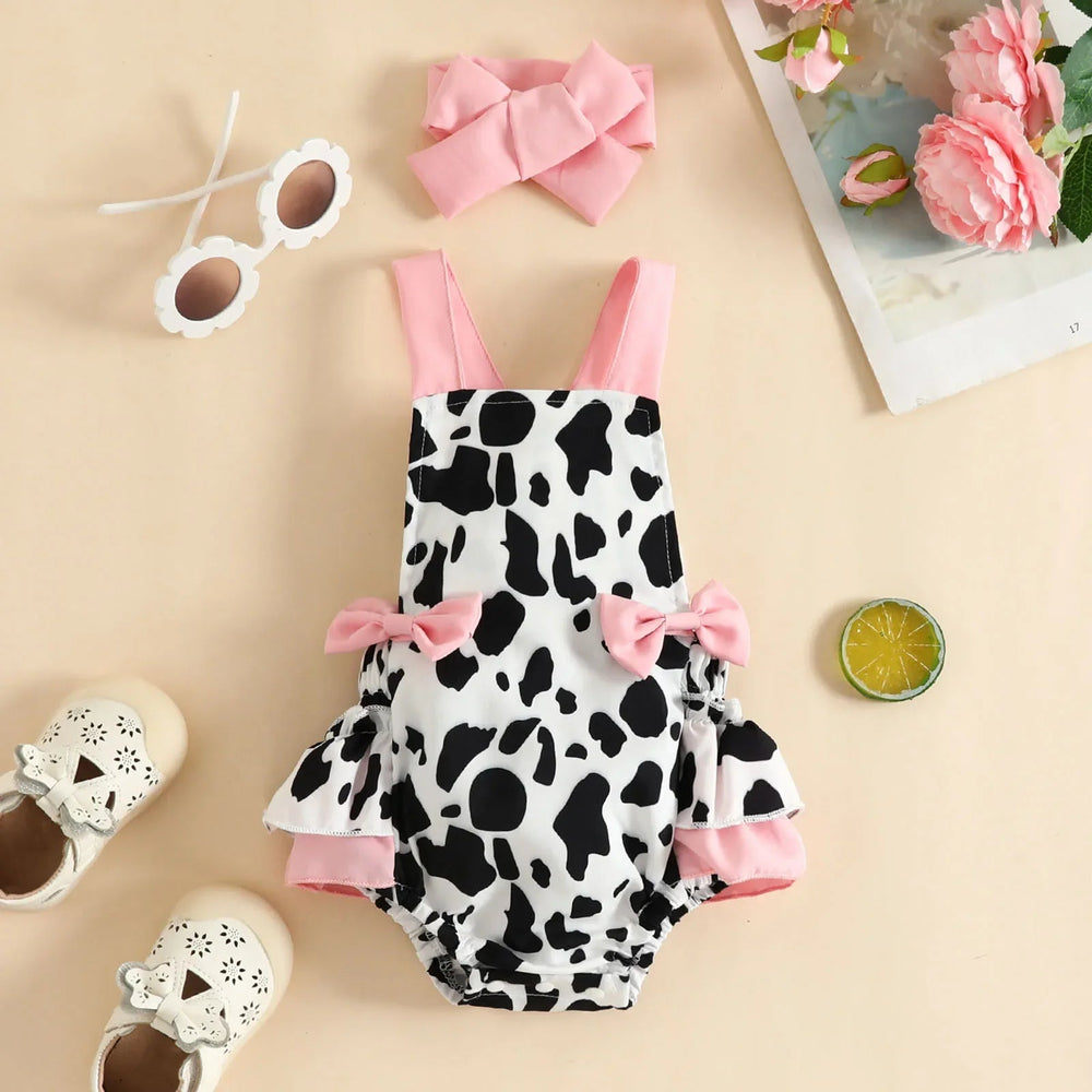 Cow-print baby romper with pink shoulder straps, side bows, ruffled trim and a matching bow headband