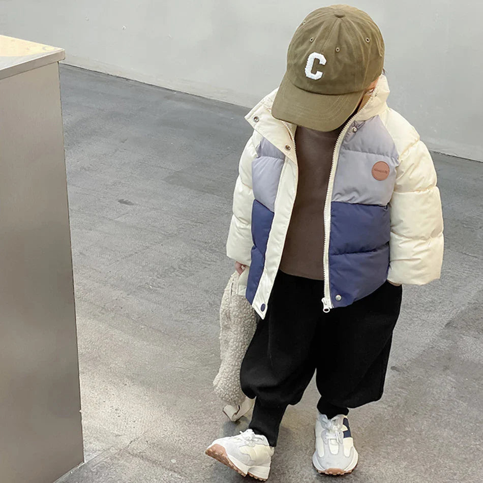 Child standing in a cream, gray, and navy color-block winter coat with the front open.