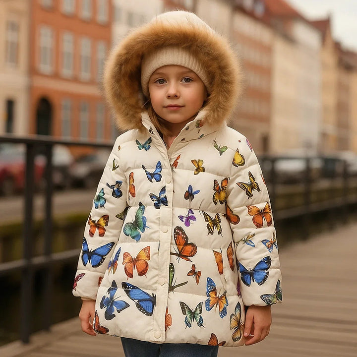 Child wearing a cream butterfly-print winter coat with fluffy hood trim on a footbridge