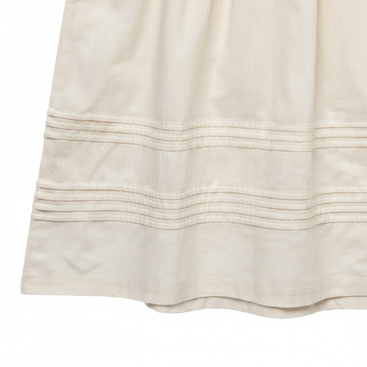 Close-up of horizontal stitched tucks along the hem of a cream dress