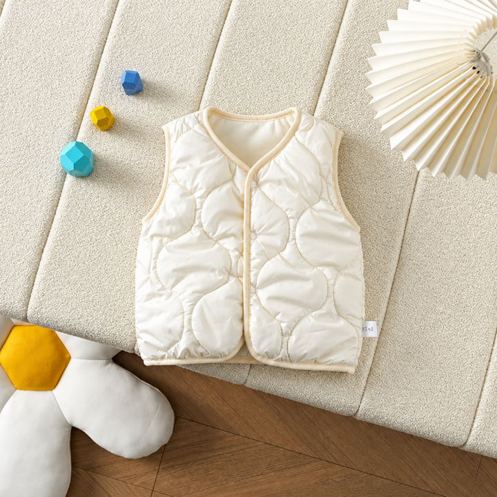 Cream quilted baby vest with front snaps laid on a cushion.