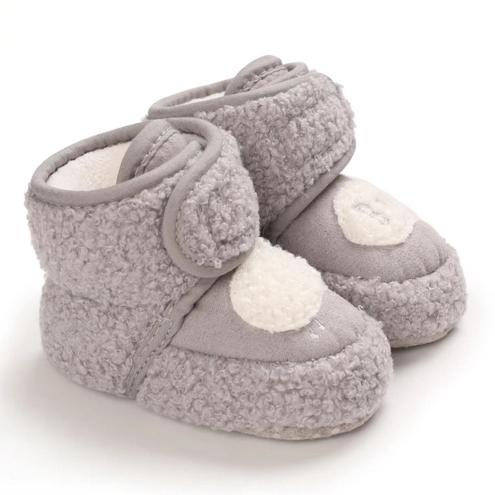 Dark gray plush baby shoes with cream toe accents and wraparound ankle straps.