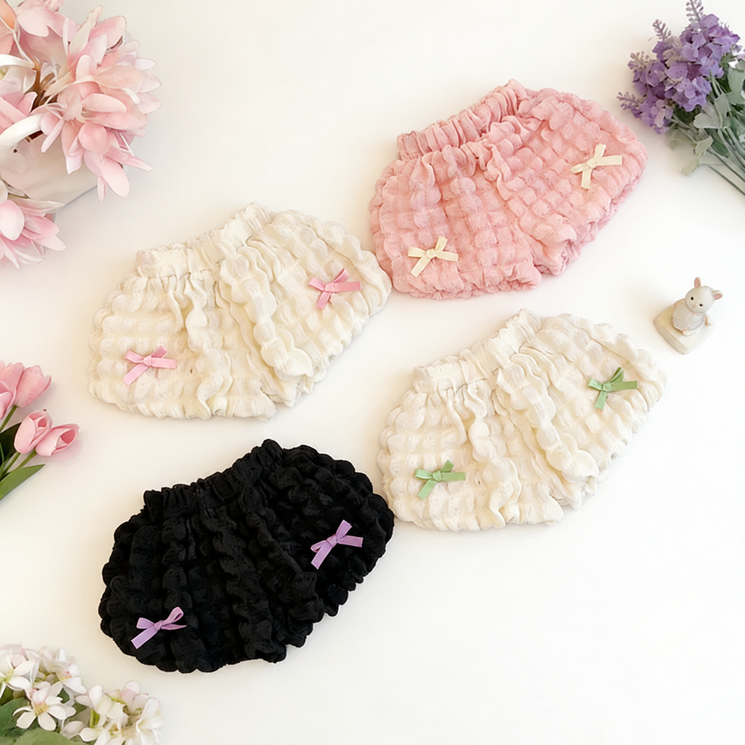 Four ruffle shorts styles arranged diagonally with pink, green, cream, and lavender bows