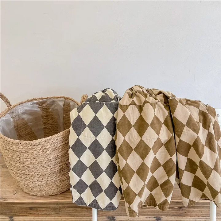 Gray and brown diamond-pattern pants draped over a wooden bench beside a woven basket