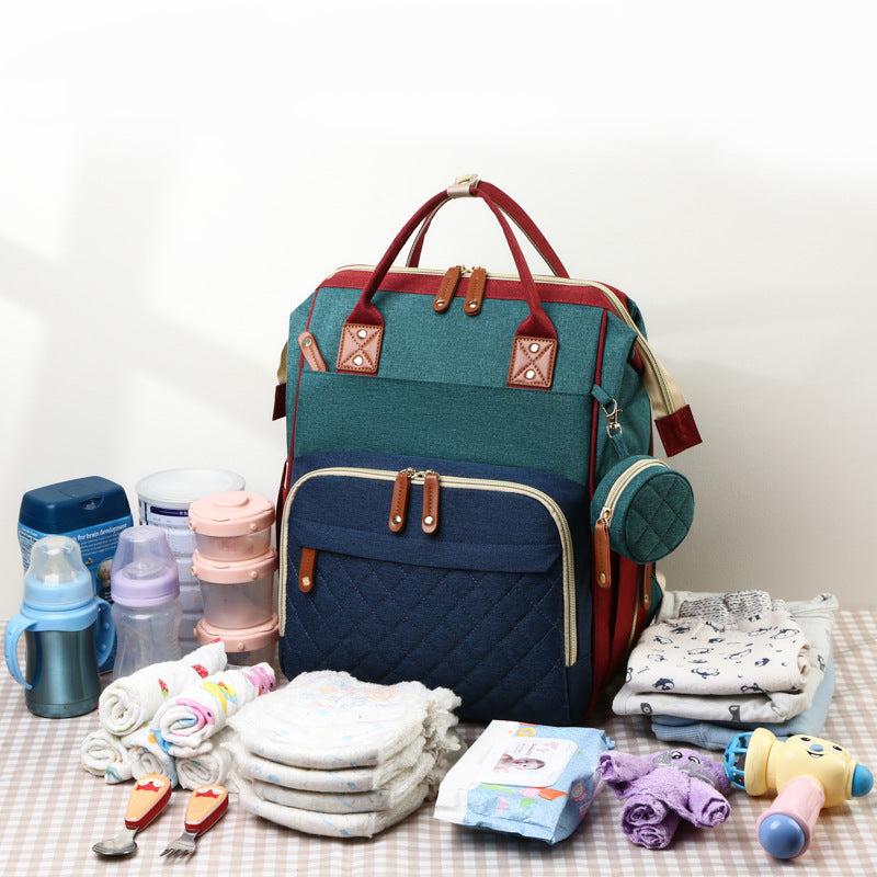 Blue-and-green diaper backpack beside bottles, diapers, wipes, clothing, and toys