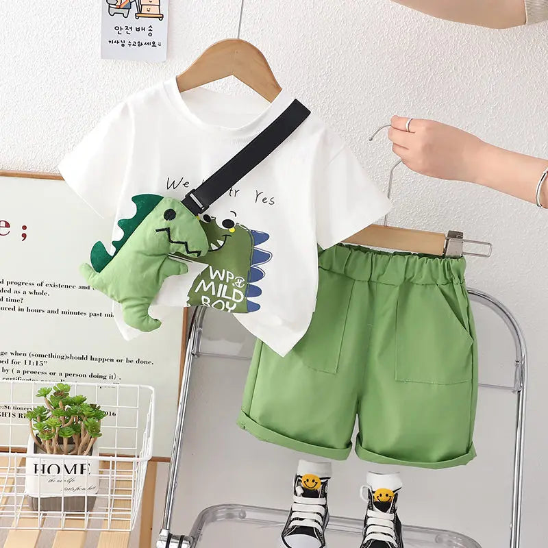 White dinosaur T-shirt and green elastic-waist shorts on hangers with a green dinosaur toy