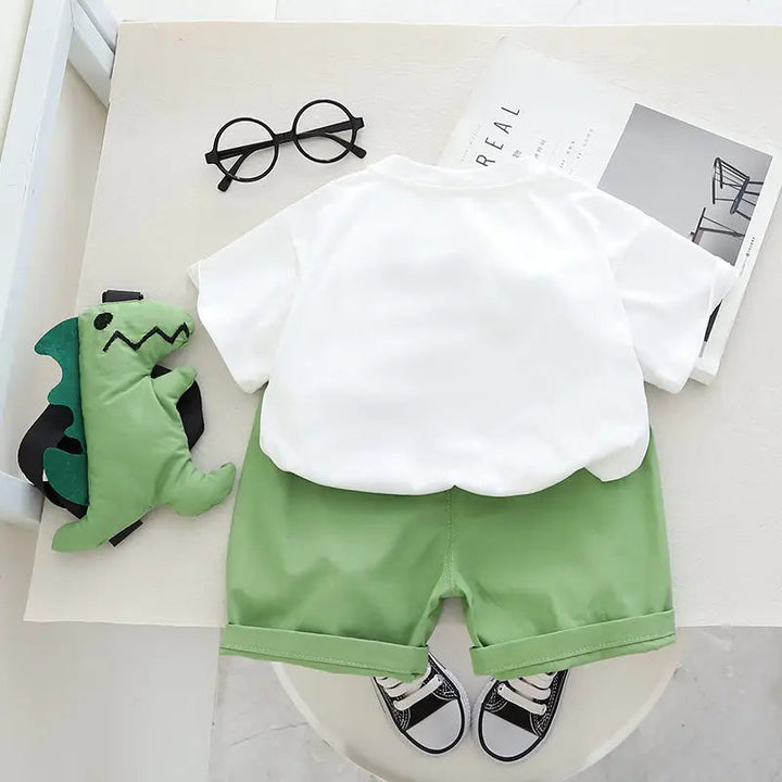 Back view of the white T-shirt and green shorts, with the dinosaur toy beside the outfit