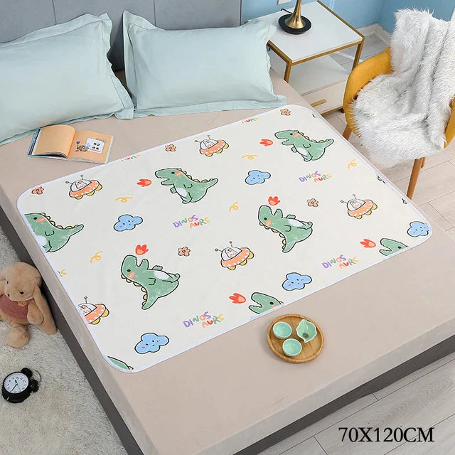 Dinosaur-print changing mat on a bed with light blue pillows, labeled 70 x 120 cm.