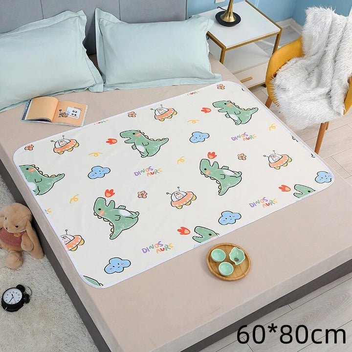 White changing mat with green dinosaurs spread across a bed, labeled 60 x 80 cm.