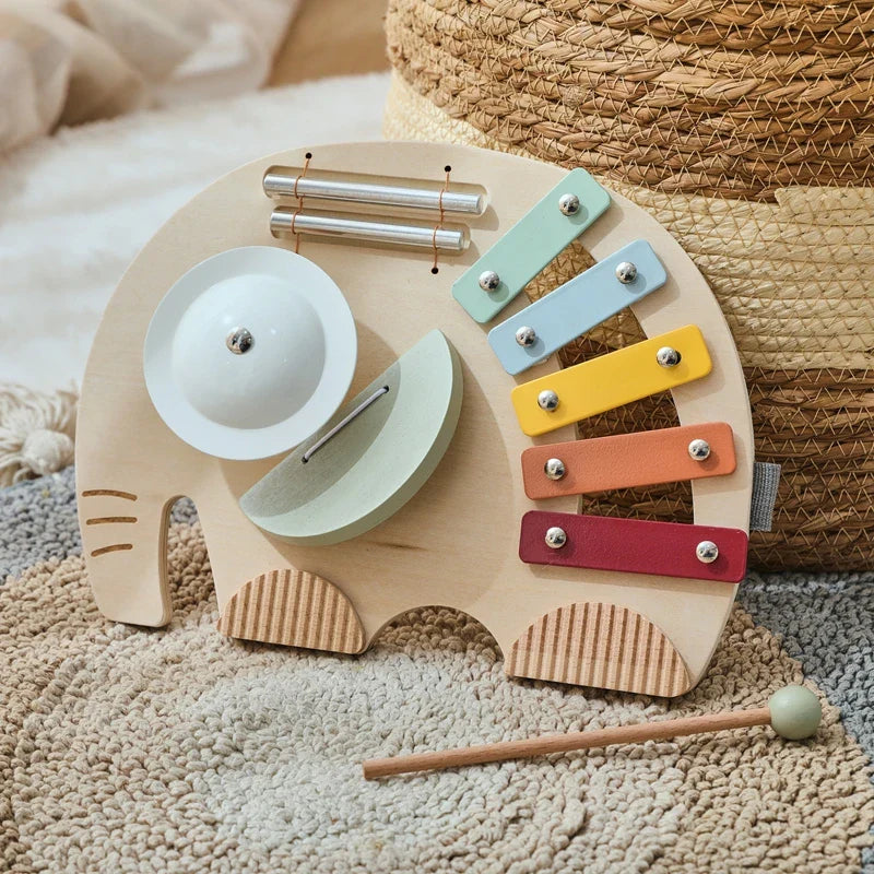 Elephant-shaped wooden xylophone with colorful bars, cymbal, chimes, and a mallet on a rug