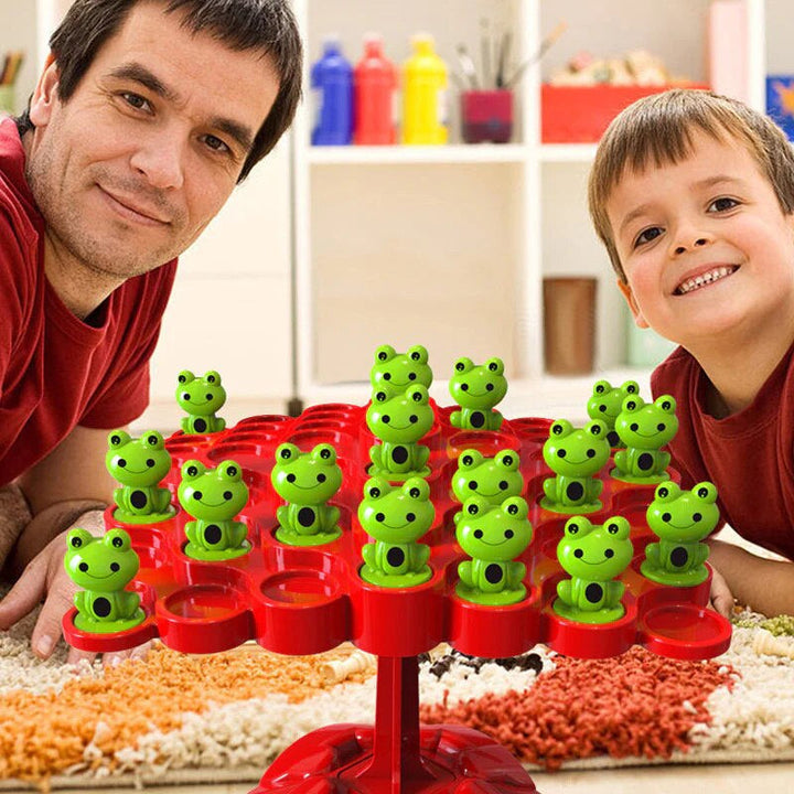 An adult and child with green frogs arranged on a red tree-shaped balancing board.