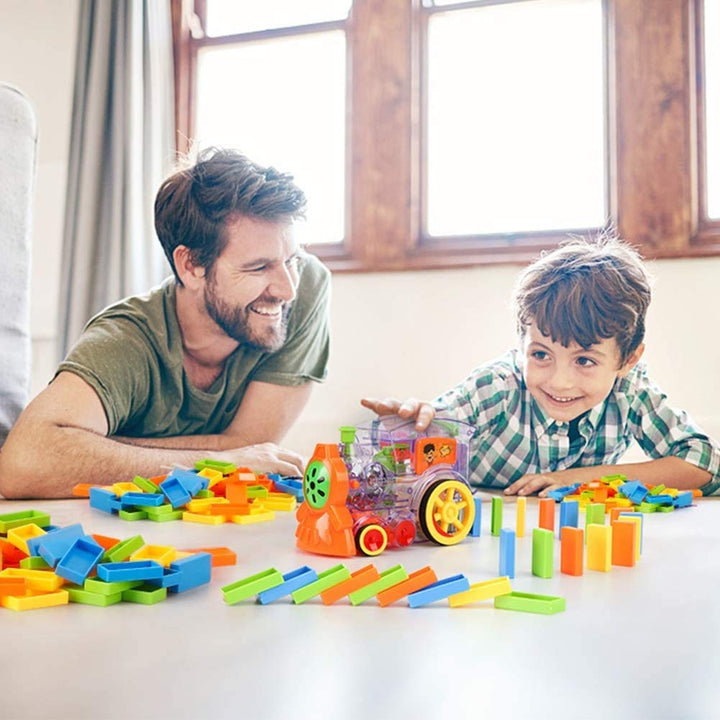 An adult and child playing with a clear toy train and colorful dominoes on a table