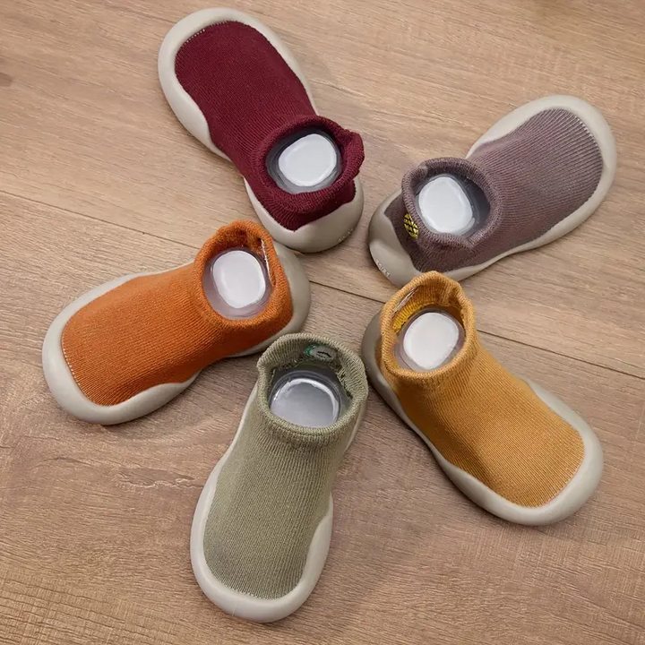 Five colors of sock-style baby shoes arranged on a wooden surface