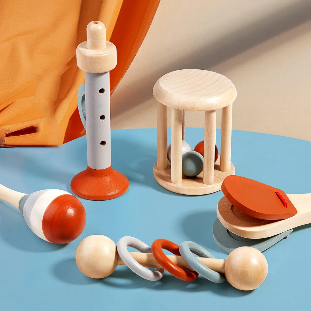 Five wooden musical toys on a blue tabletop, including rattles, a maraca, clapper and recorder-style toy
