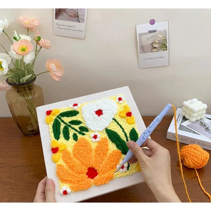 Hands creating a raised floral design with a blue punch needle pen on framed fabric.