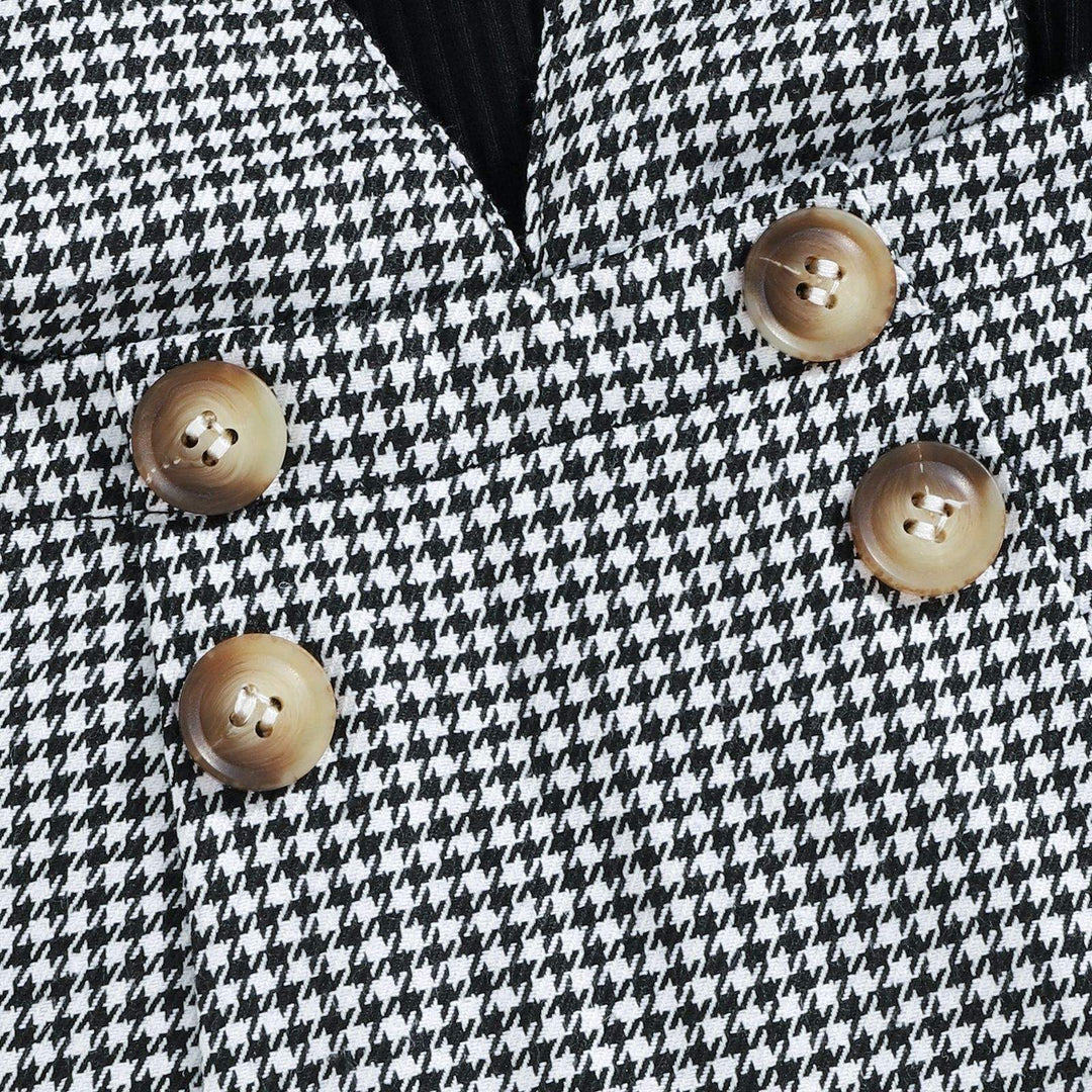 Four tan decorative buttons on the front of the black-and-white houndstooth pinafore skirt.