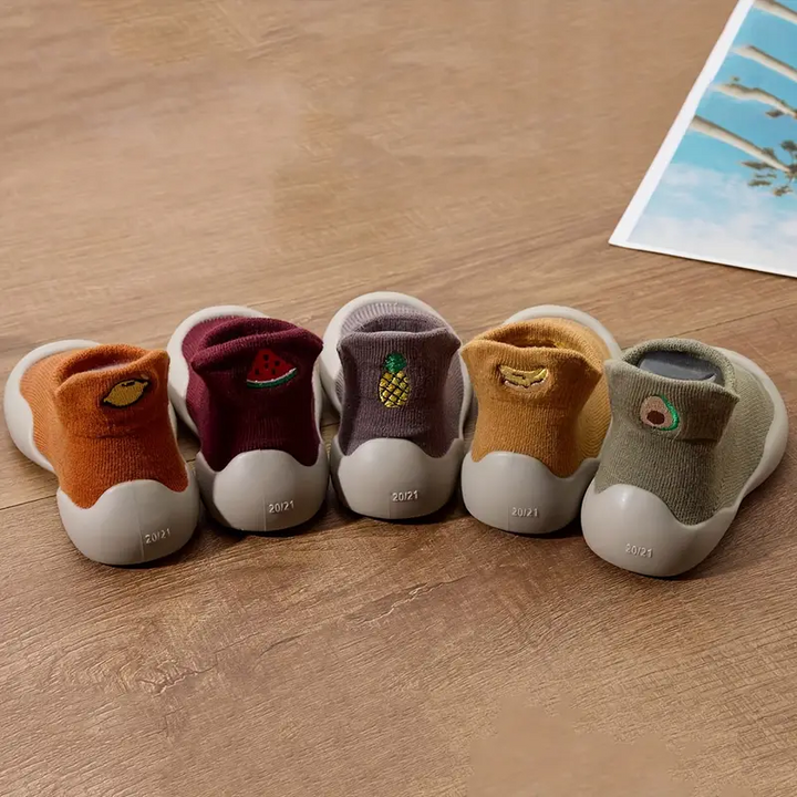 Back view of five baby shoe colors with fruit motifs above pale rubber heels