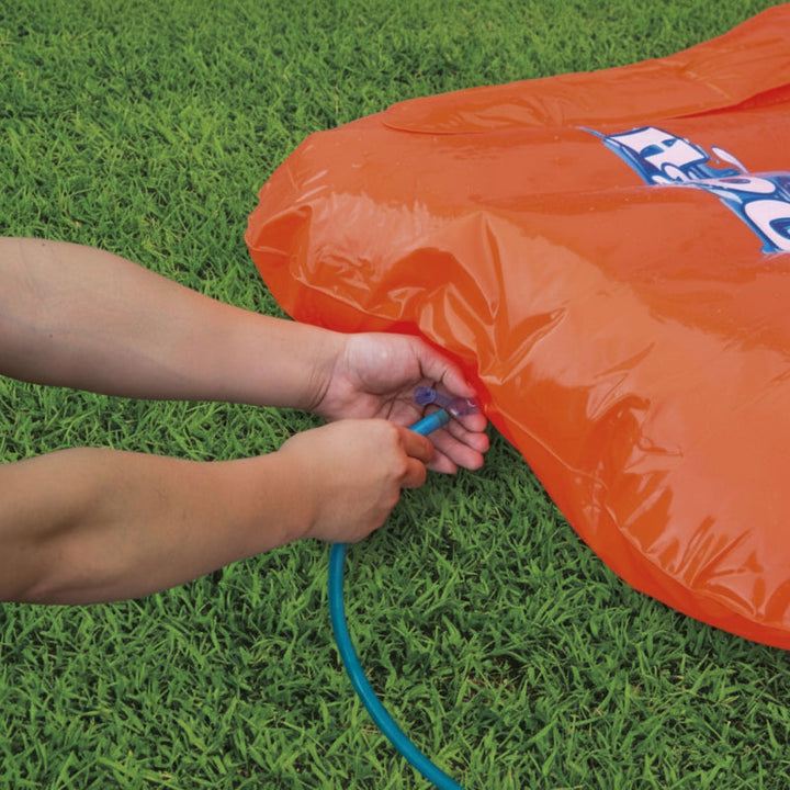 Hands connecting a garden hose beside the orange inflatable slide bumper