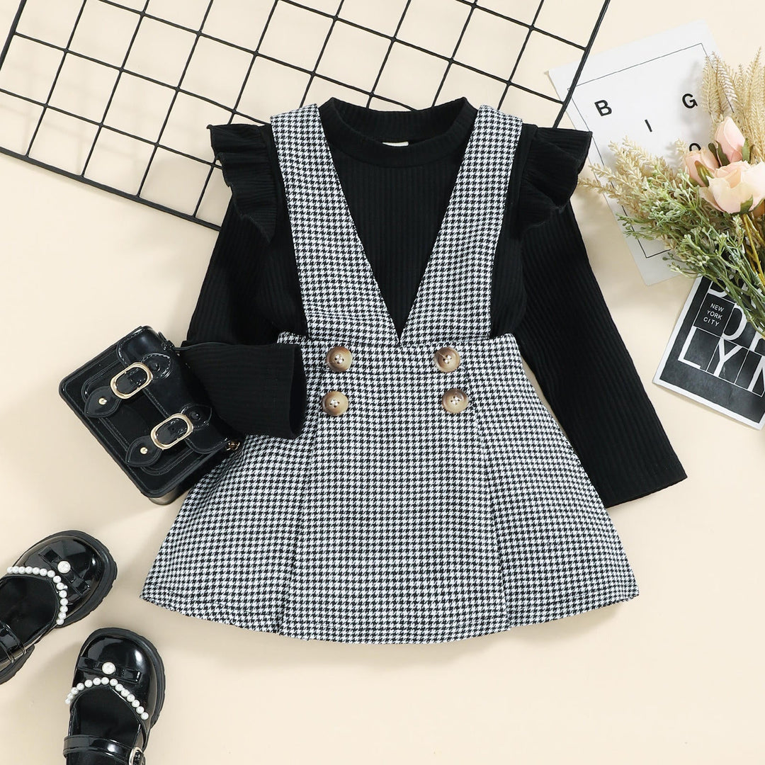 Black ruffle-shoulder top with a black-and-white houndstooth pinafore skirt and four decorative buttons.