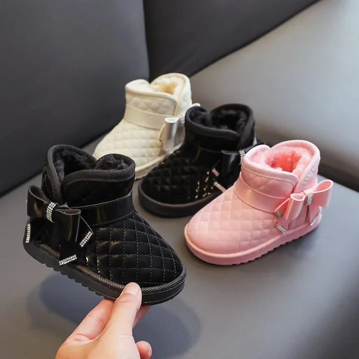 Black quilted winter boot held in front of matching pink and cream white bow-detail styles