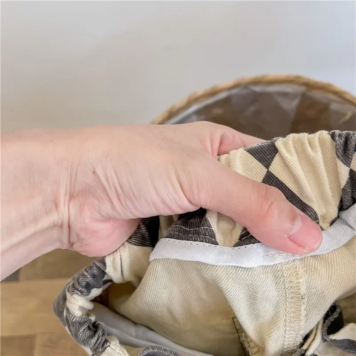 Hand holding open the waistband of gray argyle pants to show the inside stitching