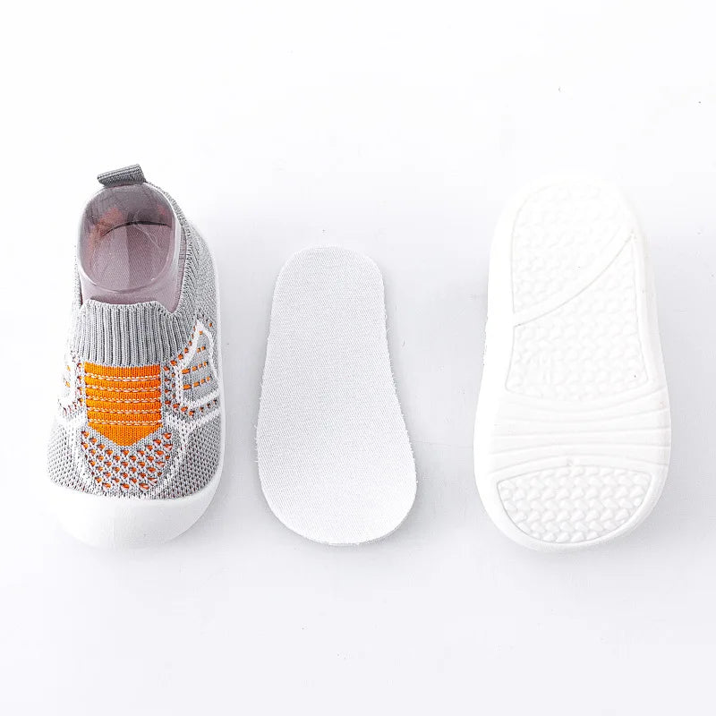 Gray knit baby shoe with orange accents beside a white insole and textured outsole