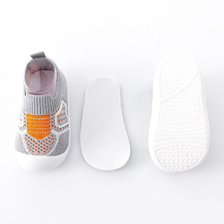 Gray knit baby shoe with orange accents beside a white insole and textured outsole
