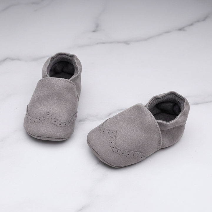 Gray baby shoes with gathered ankles and decorative toe details on a marble-patterned surface