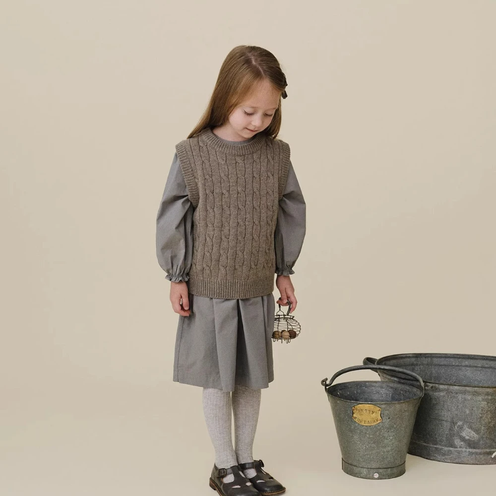 Child wearing a gray cable-knit vest over a gray dress