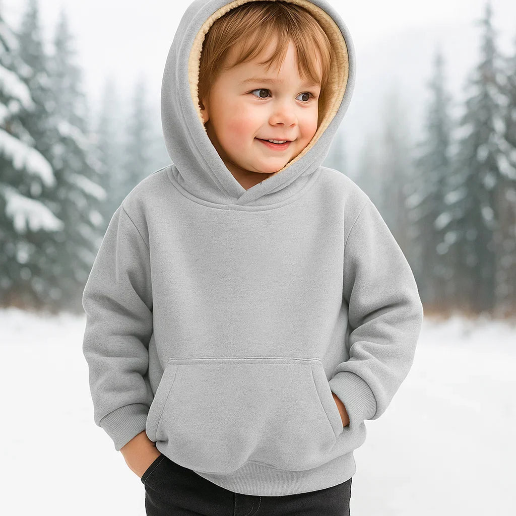 Child wearing a gray hoodie with the hood up and hands in the front pocket in a snowy setting