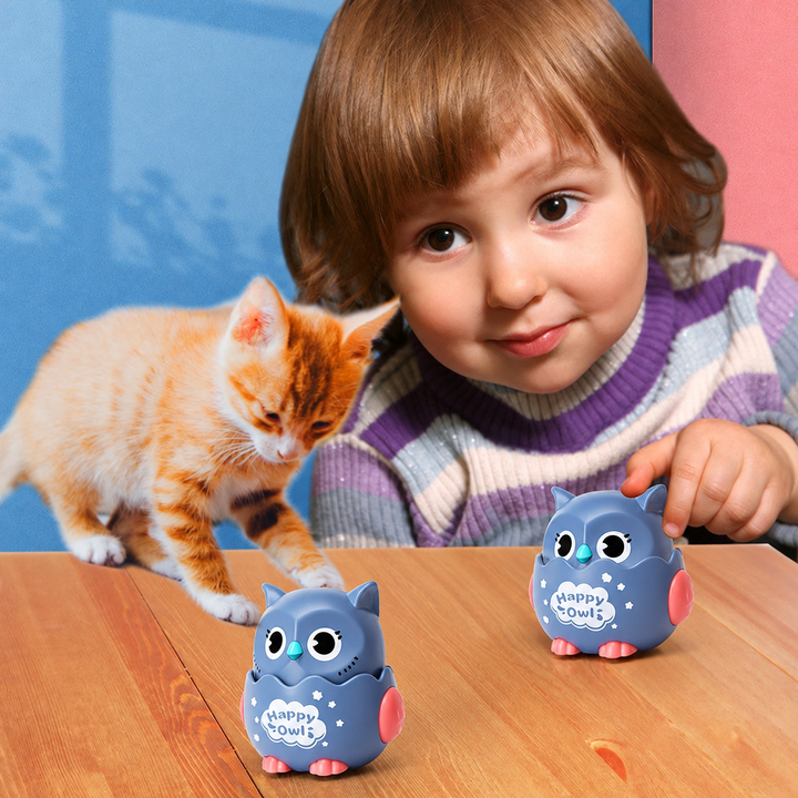 Child playing with gray owl toy cars on a wooden table beside an orange kitten.