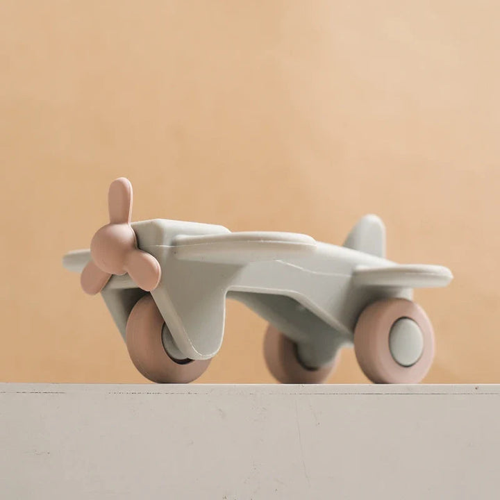 Angled view of a gray silicone toy airplane with pink wheels and a pink propeller