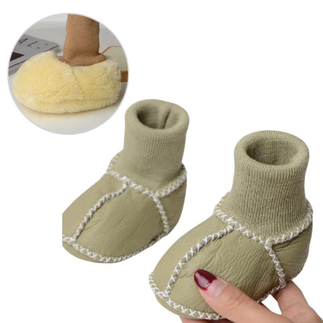 Green baby slippers held in a hand, showing knit cuffs and rounded toes