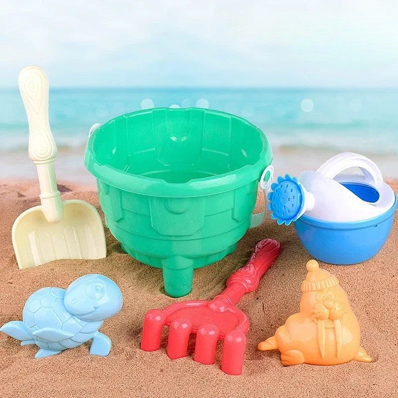 Green sandcastle bucket with a shovel, rake, blue watering can, and sea animal molds on the beach