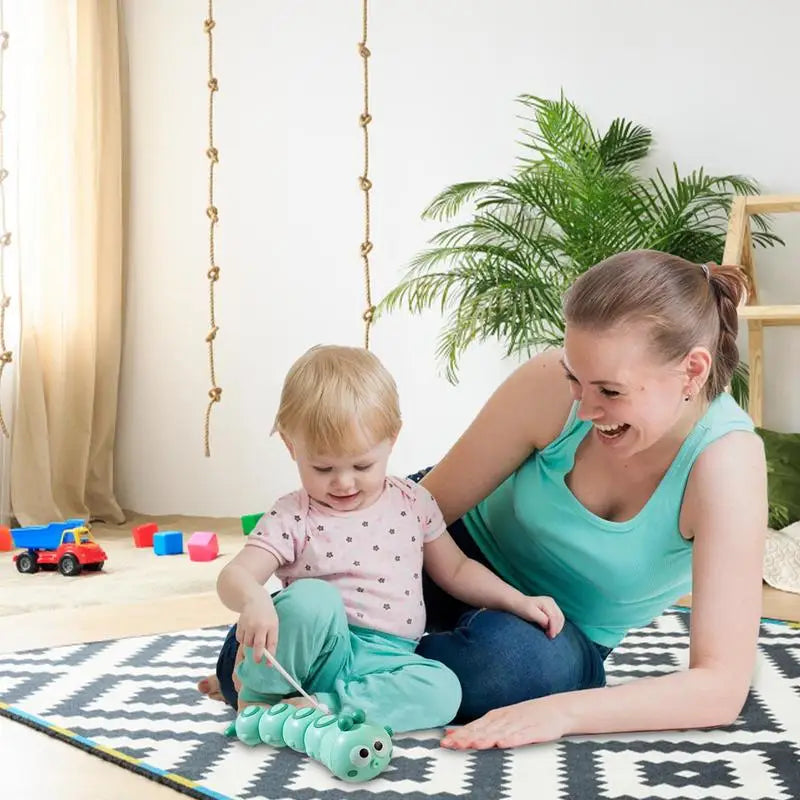 Toddler and adult playing on a rug with a green wind-up caterpillar toy