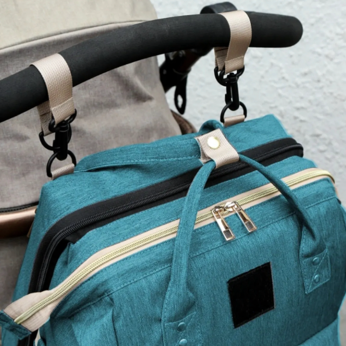 Close-up of a green diaper bag attached to a stroller handle with straps and clips.