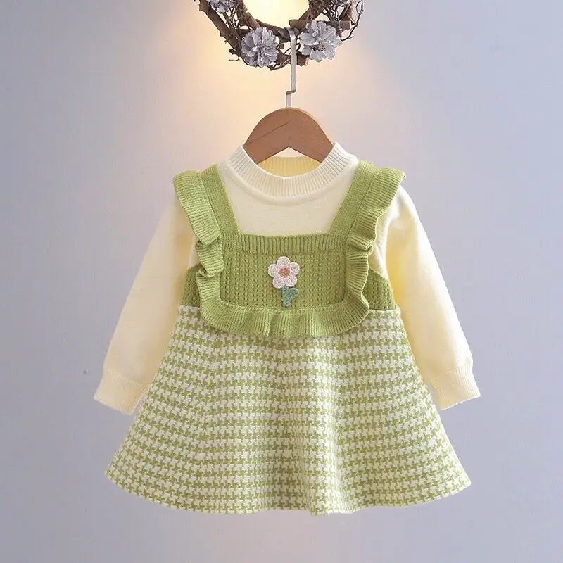 Green long-sleeve dress with ruffled trim, a small flower detail, and a houndstooth skirt